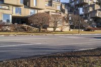 the corner of an empty street in front of some apartment buildings and a tree lined city street