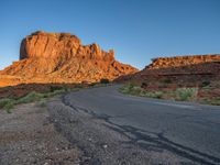 a desert road with desert and mountains in the background at sunset and sun setting on top