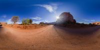 a desert road surrounded by red rock formations with blue skies overhead and sun bursting through the clouds