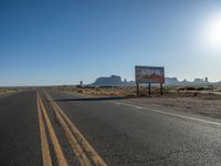 a sign is by a deserted desert road near the desert, which looks like it has no traffic