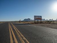 a sign is by a deserted desert road near the desert, which looks like it has no traffic