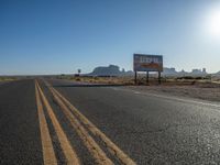 a sign is by a deserted desert road near the desert, which looks like it has no traffic