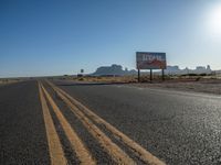 a sign is by a deserted desert road near the desert, which looks like it has no traffic