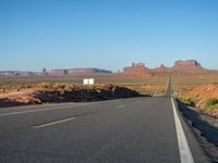 an empty road near some rocky mountains in the desert on a clear day with blue skies