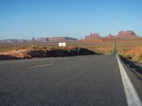 an empty road near some rocky mountains in the desert on a clear day with blue skies