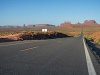 an empty road near some rocky mountains in the desert on a clear day with blue skies