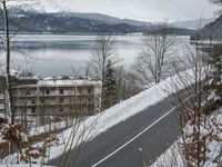 a view of a town across the water and mountains in winter time with a road going to the right