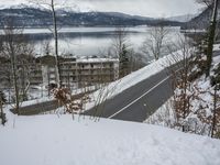 a view of a town across the water and mountains in winter time with a road going to the right