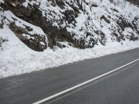 a man riding a motorcycle on a snowy street next to a steep hill with lots of snow