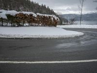 the road is surrounded by snow covered bushes and a hill in the distance is a body of water