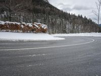 the road is surrounded by snow covered bushes and a hill in the distance is a body of water