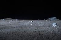 a black background shows some small rocks in a desert with dark sky behind it and a large white rock on the ground