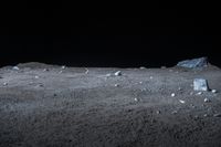 a black background shows some small rocks in a desert with dark sky behind it and a large white rock on the ground