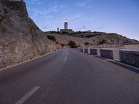 the empty road is at the end of the cliff side, with the lighthouse in the distance