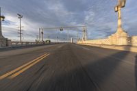 two people ride bicycles across an empty bridge on the road in the morning light, under a blue sky