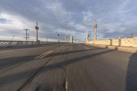 two people ride bicycles across an empty bridge on the road in the morning light, under a blue sky