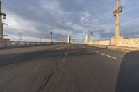 two people ride bicycles across an empty bridge on the road in the morning light, under a blue sky