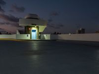 a motel sitting on a building top with a city in the background at dusk by a blue door