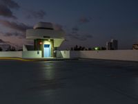 a motel sitting on a building top with a city in the background at dusk by a blue door