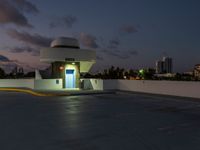 a motel sitting on a building top with a city in the background at dusk by a blue door