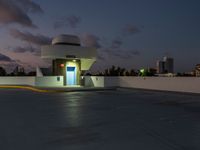 a motel sitting on a building top with a city in the background at dusk by a blue door