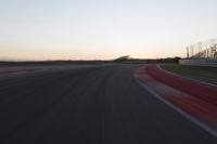 the motion blurs as the lights go on on a race track while the sun sets