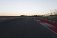 the motion blurs as the lights go on on a race track while the sun sets