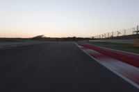 the motion blurs as the lights go on on a race track while the sun sets