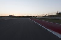 the motion blurs as the lights go on on a race track while the sun sets