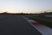 the motion blurs as the lights go on on a race track while the sun sets