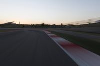 the motion blurs as the lights go on on a race track while the sun sets