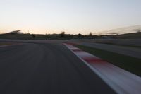 the motion blurs as the lights go on on a race track while the sun sets