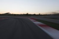 the motion blurs as the lights go on on a race track while the sun sets