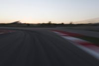 the motion blurs as the lights go on on a race track while the sun sets