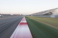 motion blurry photograph of a racing track during the day or night, with green grass, gravel and red stripes on the bottom