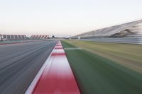 motion blurry photograph of a racing track during the day or night, with green grass, gravel and red stripes on the bottom