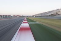 motion blurry photograph of a racing track during the day or night, with green grass, gravel and red stripes on the bottom