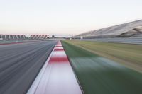 motion blurry photograph of a racing track during the day or night, with green grass, gravel and red stripes on the bottom