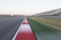 motion blurry photograph of a racing track during the day or night, with green grass, gravel and red stripes on the bottom