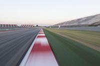 motion blurry photograph of a racing track during the day or night, with green grass, gravel and red stripes on the bottom