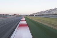 motion blurry photograph of a racing track during the day or night, with green grass, gravel and red stripes on the bottom