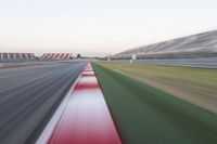 motion blurry photograph of a racing track during the day or night, with green grass, gravel and red stripes on the bottom