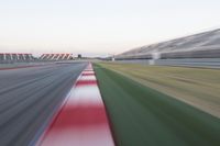 motion blurry photograph of a racing track during the day or night, with green grass, gravel and red stripes on the bottom