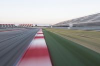 motion blurry photograph of a racing track during the day or night, with green grass, gravel and red stripes on the bottom