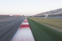 motion blurry photograph of a racing track during the day or night, with green grass, gravel and red stripes on the bottom