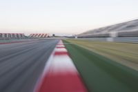 motion blurry photograph of a racing track during the day or night, with green grass, gravel and red stripes on the bottom