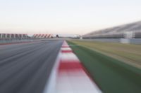 motion blurry photograph of a racing track during the day or night, with green grass, gravel and red stripes on the bottom