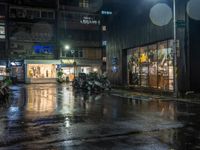 motor bikes are parked on a city street in the rain, which is dark at night