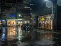 motor bikes are parked on a city street in the rain, which is dark at night