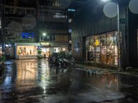 motor bikes are parked on a city street in the rain, which is dark at night